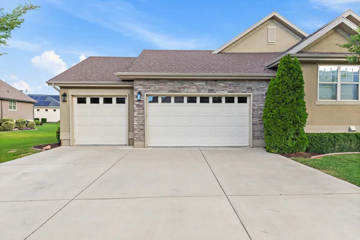 Two-car garage with panel doors, stone veneer accents, and stucco exterior