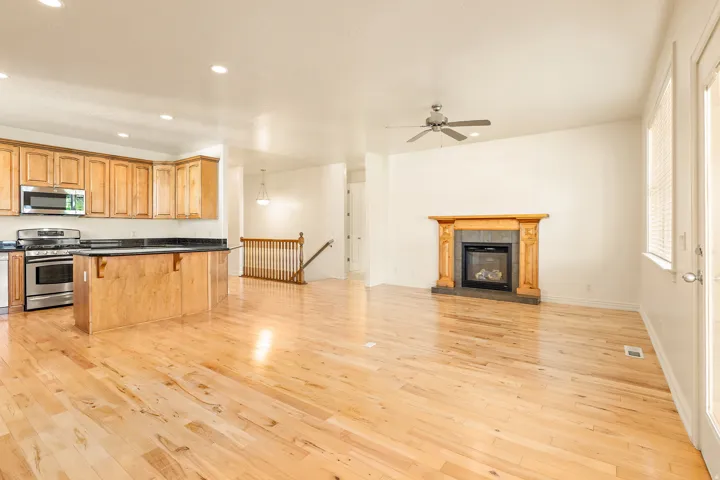 Open-concept living area with wood-finish flooring, a kitchen island with dark countertops, stainless steel appliances, and a fireplace with a decorative mantel