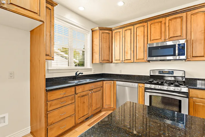 Wood-finish cabinetry, dark speckled countertops, undermount sink with a matte black faucet, stainless steel appliances, and recessed lighting