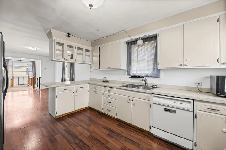 Kitchen – Sink & Storage – Generous counter space wraps around a double basin sink, complemented by a full wall of cabinetry and included dishwasher.