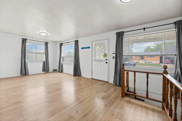 Entry / Living Area – Multiple large windows and a paneled front door bring in abundant natural light, while the wood stair railing adds warmth to this welcoming entry-level space.