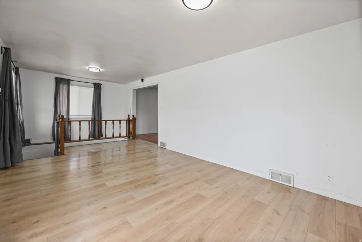 Living Room / Entry – A bright, open living space finished with wide-plank laminate flooring, a wood-accented stair railing, and a large curtained window that fills the room with natural light.