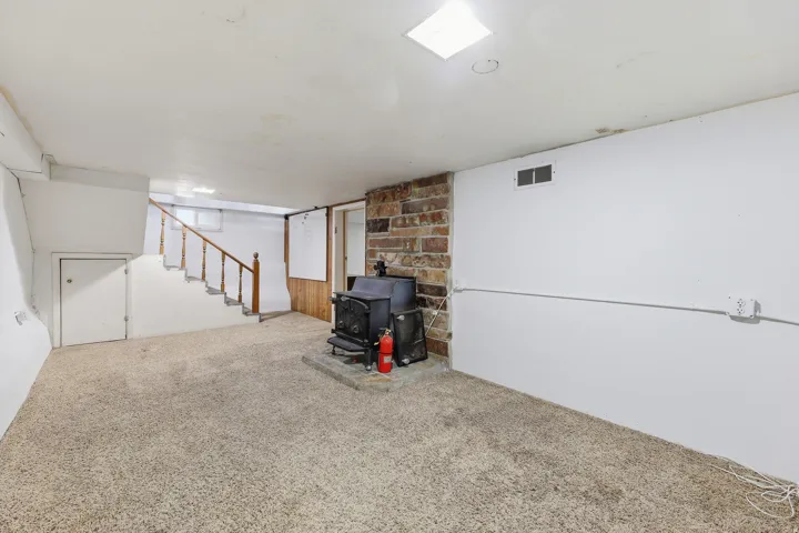 Basement Stairwell Area – Additional finished basement square footage with a wood-burning stove set against a stone surround, plus access to the exterior and storage below the stairs.