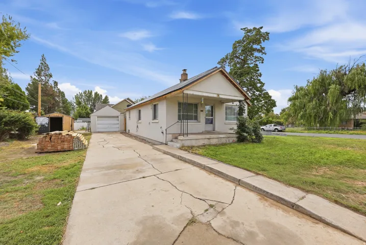 Front Exterior – This classic stucco bungalow features a metal roof, covered front porch, and detached garage, all set on a spacious corner lot with mature landscaping.