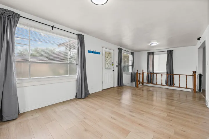 Living Room / Entry – Bright, open living space featuring warm wood-look flooring, large windows, and abundant natural light. The room flows naturally toward the entry and adjoining areas, creating a comfortable gathering space.