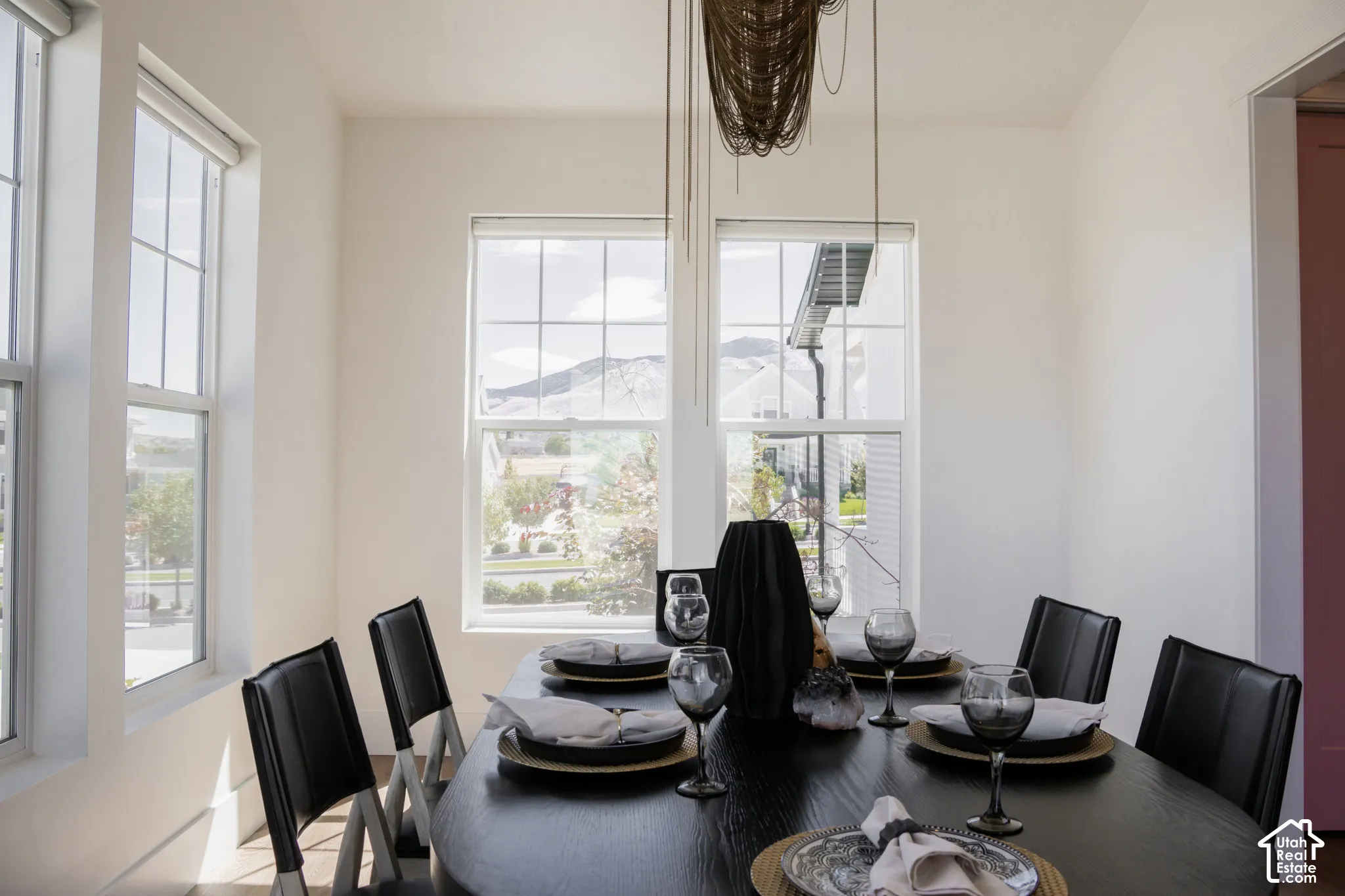 Dining area with multiple windows, featuring light-toned walls and a linear chandelier