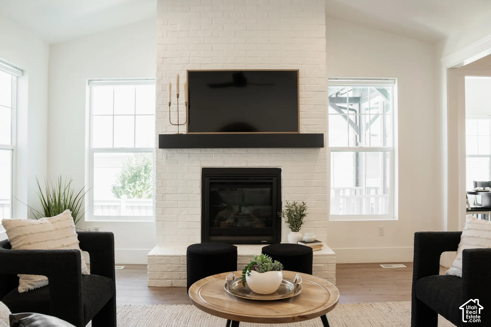 Vaulted ceilings complemented by a white brick fireplace with a black mantel and integrated firebox