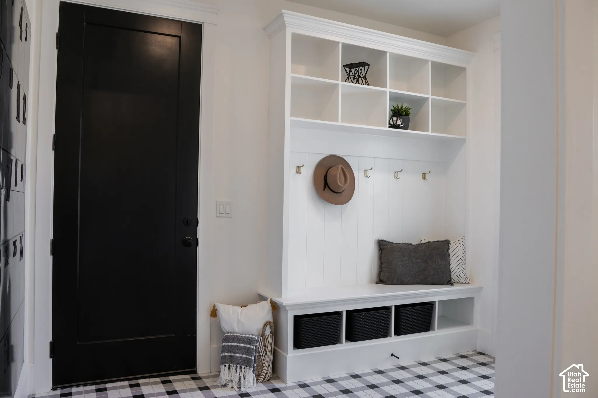 Built-in white mudroom bench with upper shelving and coat hooks, set against a black and white checkered floor
