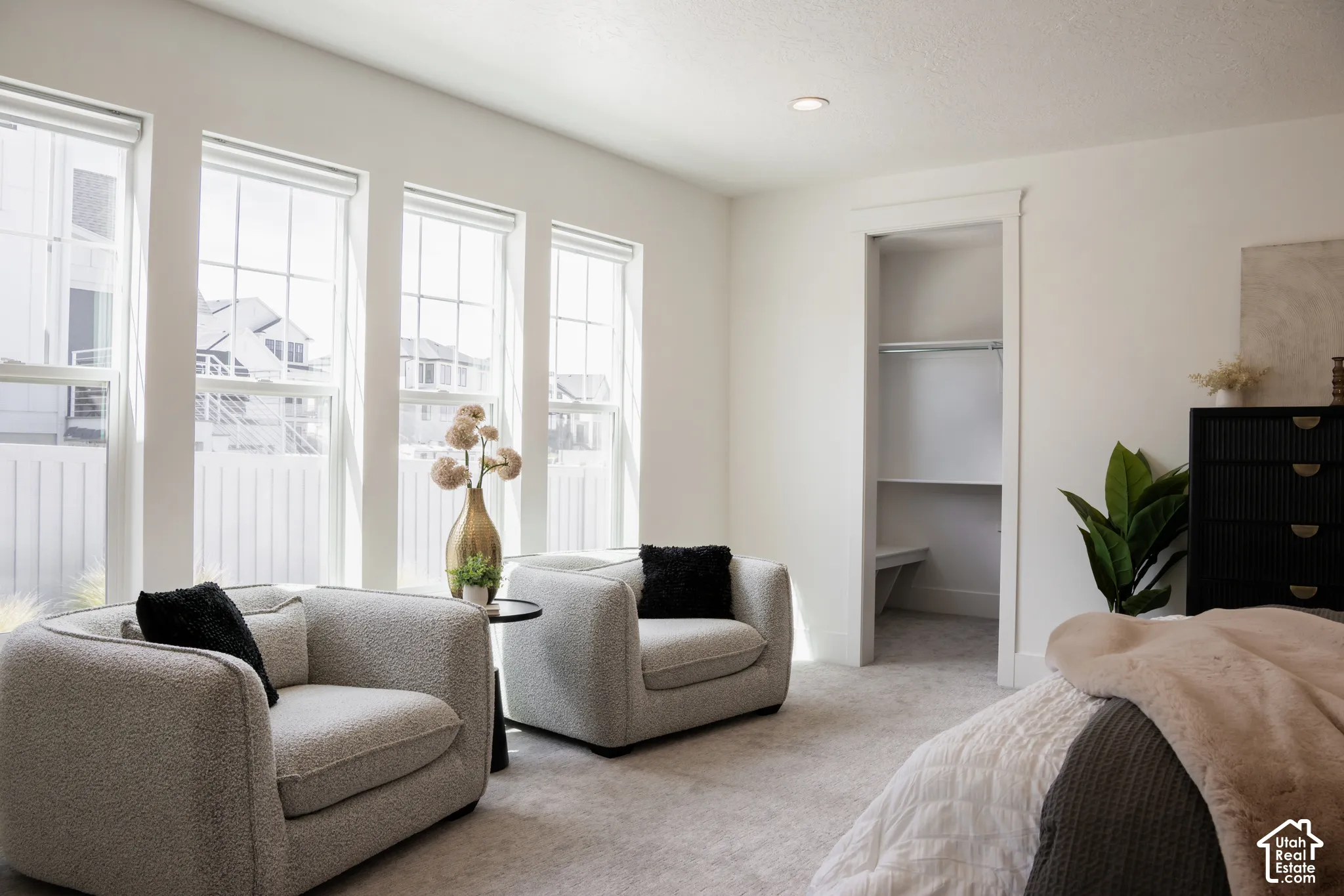 White walls, recessed ceiling lighting, light-colored carpeting, multiple windows with white frames, and a built-in closet with shelving and hanging rod