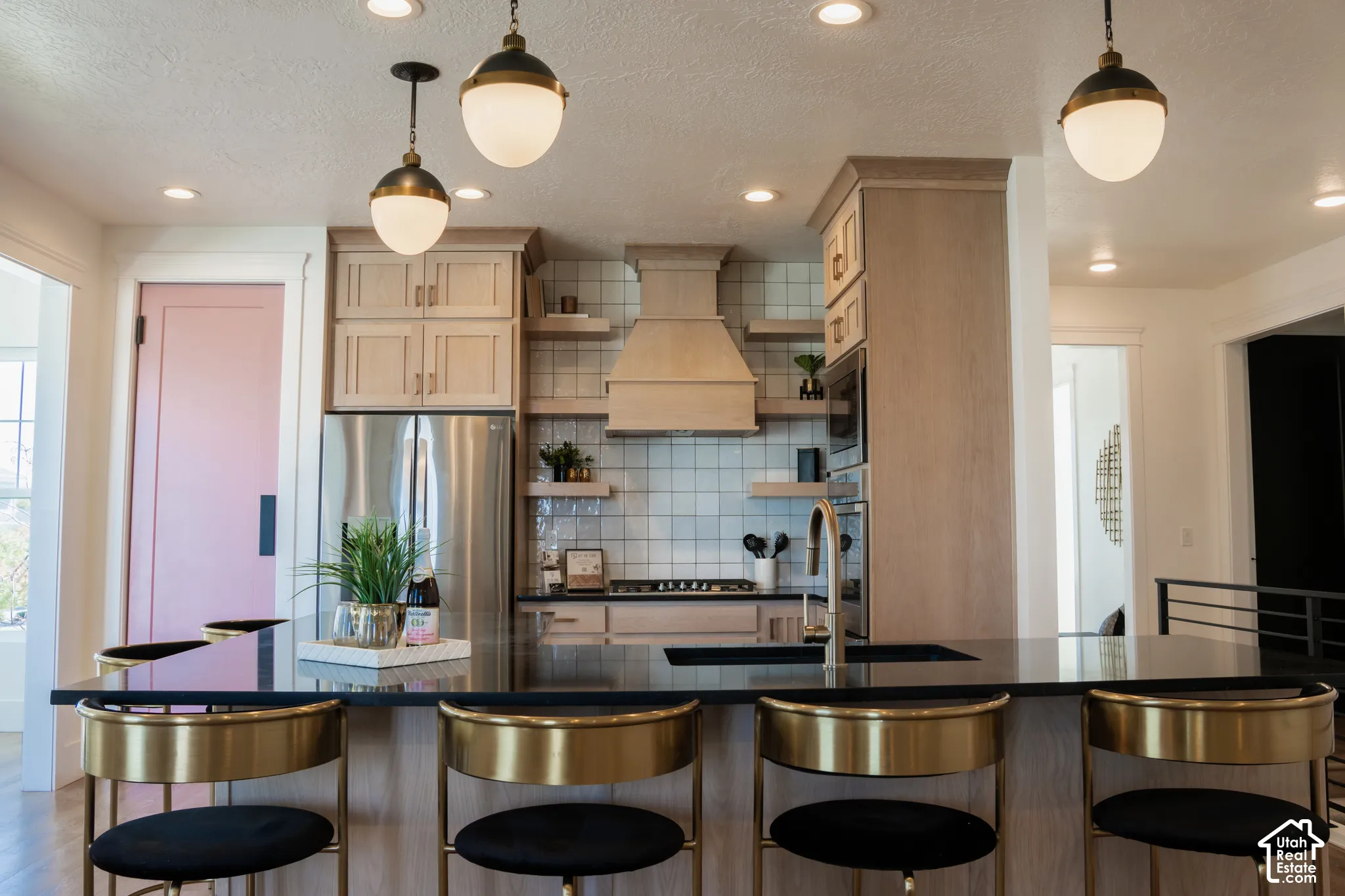 Spacious kitchen featuring an island with a dark countertop, brass pendant lighting, built-in stainless steel appliances, and light wood cabinetry