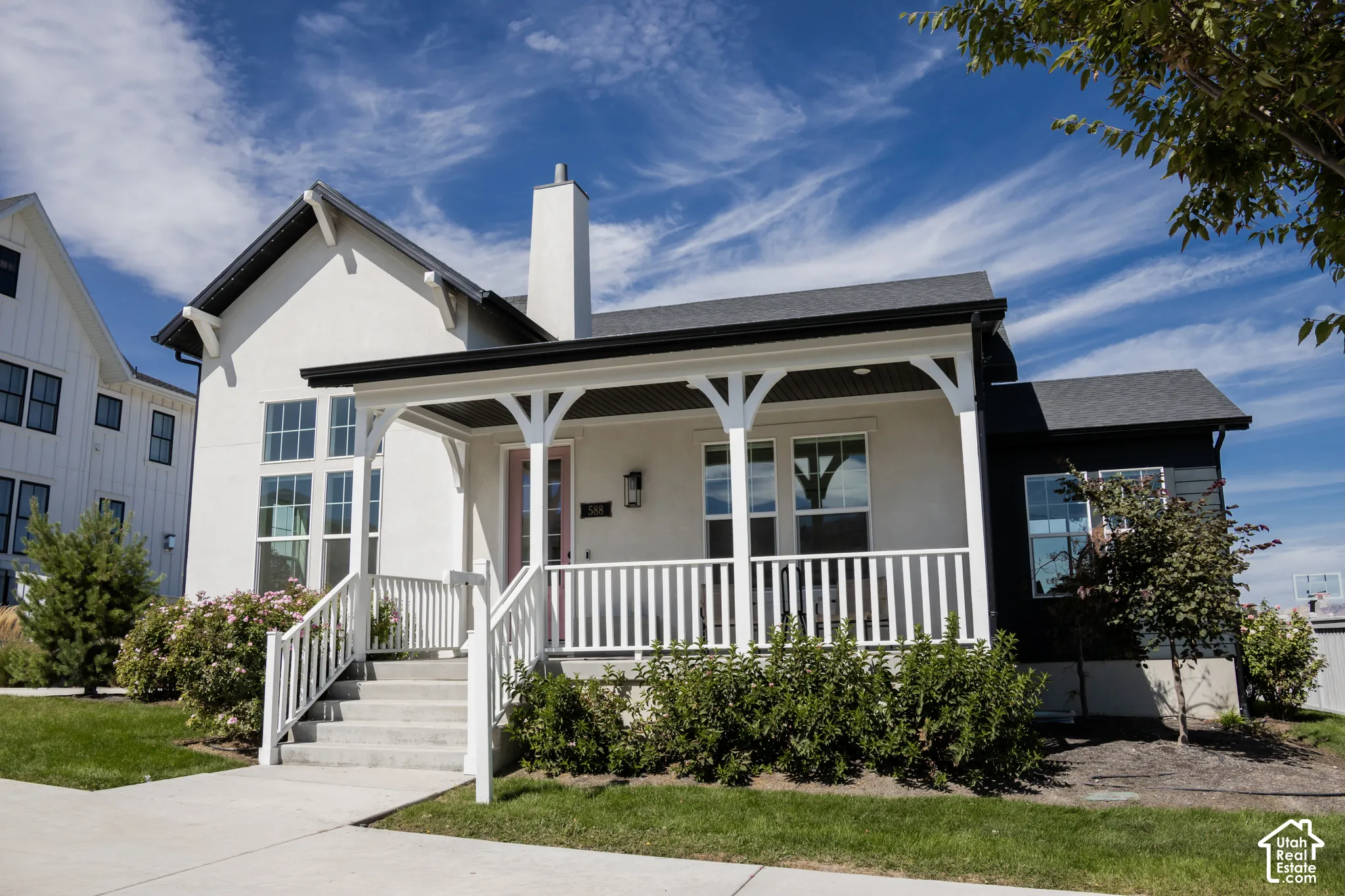 Contemporary architectural style featuring a covered porch with white railings, a contrasting black roof, a prominent chimney, and a multi-pane window design