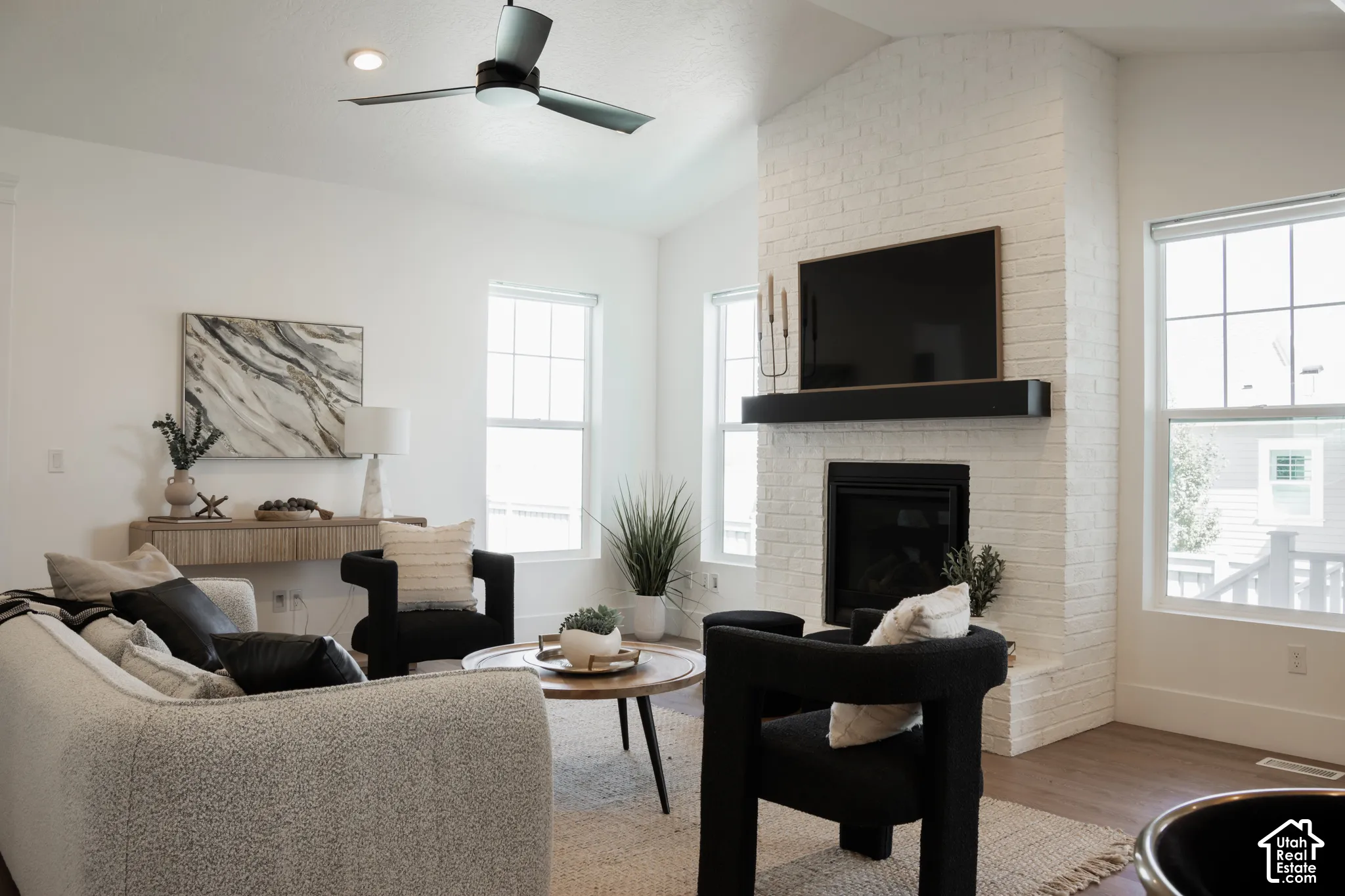 Spacious living area featuring a white brick fireplace with a wood mantel, multiple windows, recessed lighting, and wood-finish flooring
