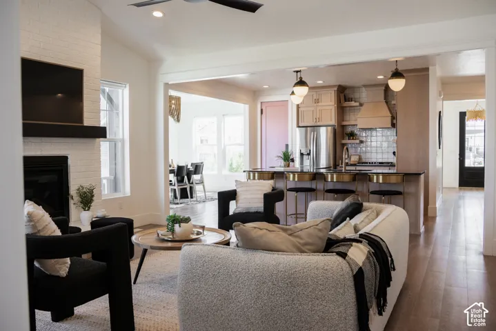 Open-concept living area featuring a white brick fireplace, wood-finish flooring, and a kitchen island with built-in bar seating
