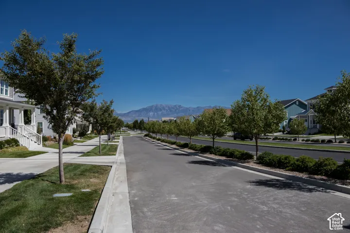 Tree-lined street with sidewalks, manicured lawns, and mountain backdrop