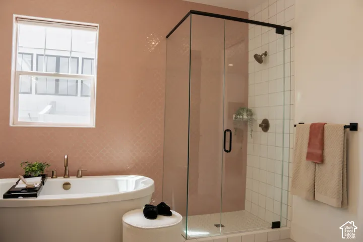 Freestanding soaking tub with brass fixtures, glass-enclosed shower with subway tile, patterned accent wall, and matte black hardware throughout