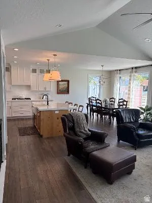 Open-concept living area with vaulted ceilings, wood-finish flooring, a kitchen island with seating, white shaker cabinetry, and recessed lighting