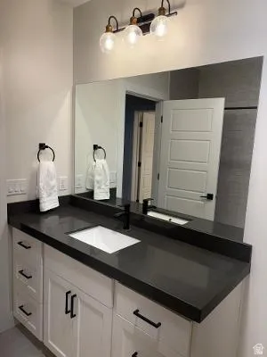 Vanity featuring a dark countertop, white shaker-style cabinetry, and matte black hardware