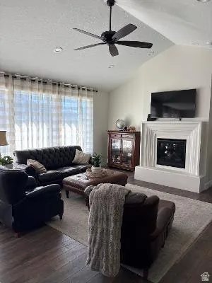 Vaulted ceiling with a ceiling fan, fireplace with a decorative mantel, recessed lighting, and wood-finish flooring