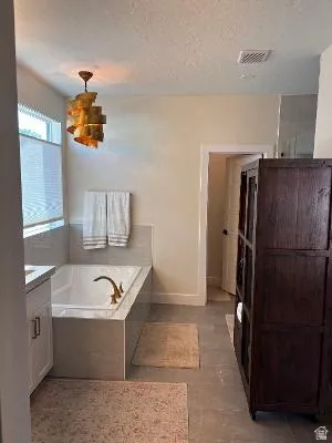 Soaking tub with a brass-finish faucet, custom vanity with undermount sink, and recessed lighting
