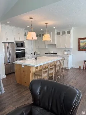 Kitchen featuring a wood-finish island with seating, white shaker cabinetry, stainless steel appliances, and wood-finish flooring