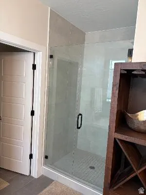 Glass-enclosed shower with a tiled interior, a dark-toned shower drain, and a black handle