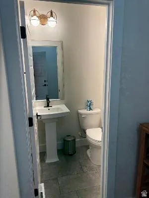 Pedestal sink with black-finish faucet, wall-mounted light fixture, and tile flooring