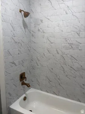 Tub-shower combination featuring subway tile with varied veining, a bronze-finish shower head, and matching bronze-finish fixtures