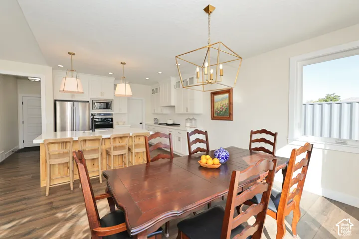 Kitchen featuring white shaker cabinetry, a stone-finish island countertop, built-in stainless steel appliances, geometric gold-tone pendant lighting, and wood-finish flooring