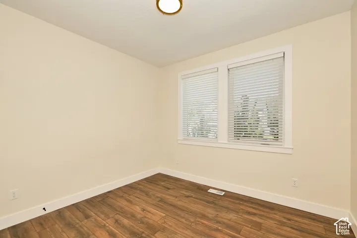 Interior room featuring wood-finish flooring, dual windows with horizontal blinds, and a circular flush-mount ceiling light fixture