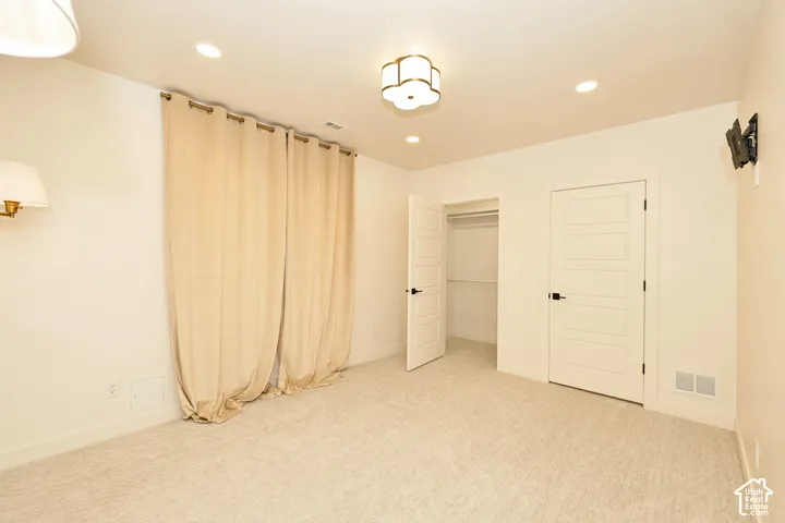 Neutral-toned interior featuring wall-to-wall carpeting, recessed lighting, a multi-paneled flush interior door, a walk-in closet with built-in shelving, and a decorative semi-flush mount light fixture