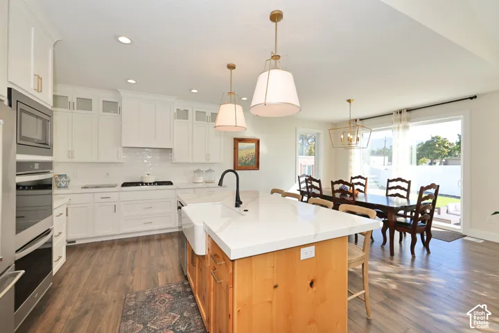 Kitchen featuring white shaker-style cabinetry, wood-finish flooring, a central island with a farmhouse sink and stone-finish countertop, stainless steel double wall ovens, and recessed lighting