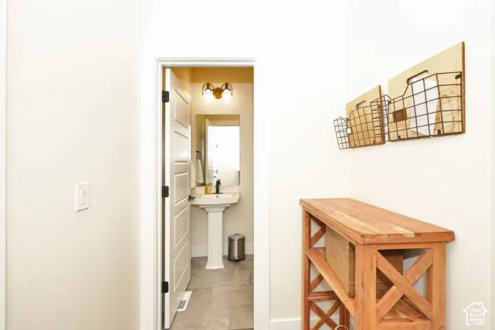 Pedestal sink with a wall-mounted mirror, two-light vanity fixture, and stone-tile flooring