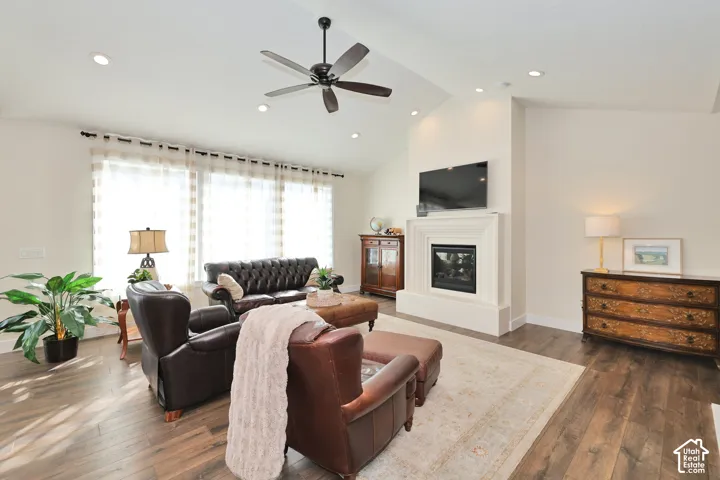 Vaulted ceilings featuring recessed lighting, a fireplace with a stepped surround, wood-finish flooring, and a ceiling fan