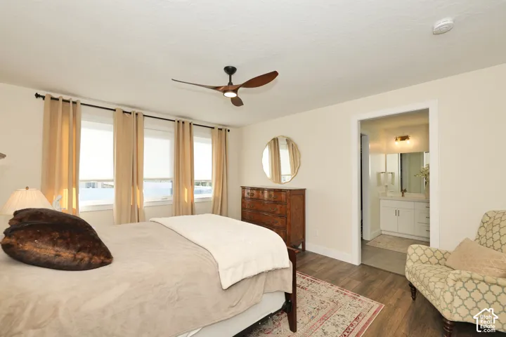Room featuring wood-finish flooring, a contemporary three-blade ceiling fan, multiple windows with neutral drapery, and a white vanity with hardware in an attached bathroom