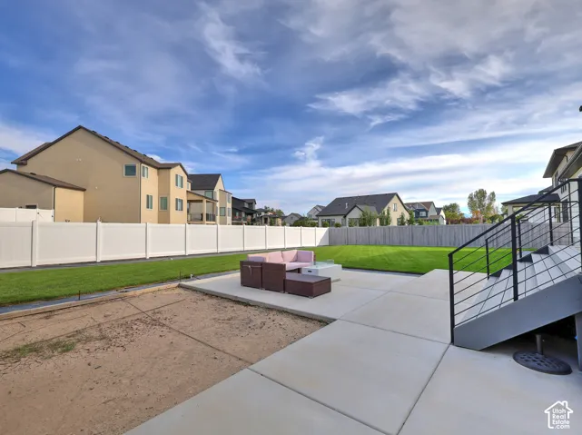 Backyard featuring a concrete patio, perimeter vinyl fencing, and a manicured lawn, complemented by a metal staircase with horizontal railing