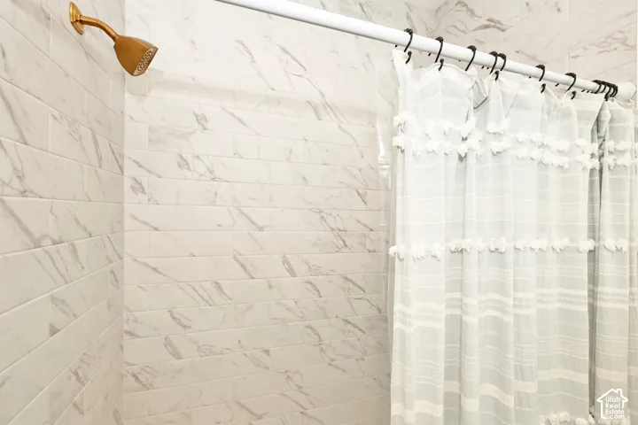 Subway-style wall tile with a veined pattern, brass-finish shower head, and an adjustable white shower curtain rod