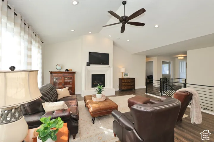 Vaulted ceilings featuring recessed lighting and a central ceiling fan, anchored by a prominent fireplace with a tiered mantel and wood-finish flooring throughout