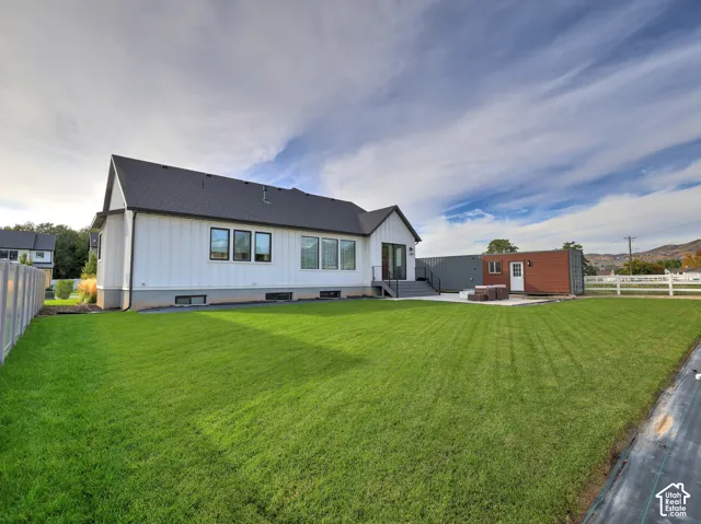 Backyard featuring a manicured lawn, white vinyl fencing, concrete patio, and a separate structure with wood-finish siding