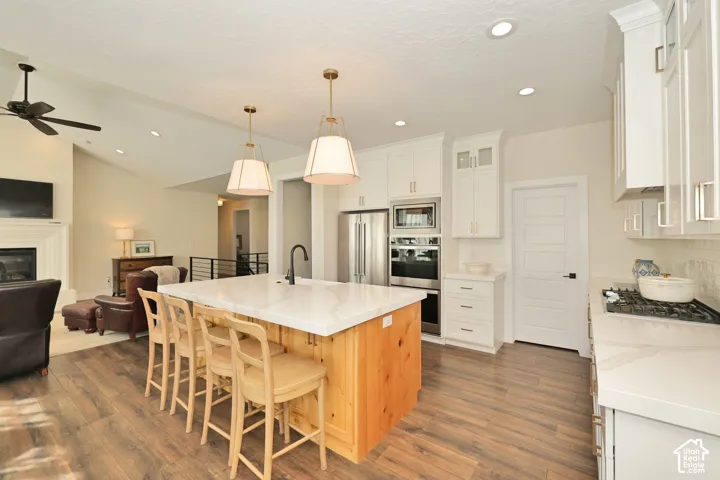 Kitchen featuring a central island with a stone-surface countertop, white cabinetry, integrated stainless steel appliances, recessed lighting, and wood-finish flooring