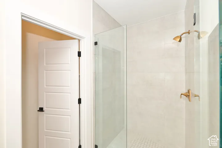 Walk-in shower featuring a glass enclosure, large-format neutral wall tile, square mosaic floor tile, and gold-finish plumbing fixtures, accompanied by a white four-panel door with matte black hardware
