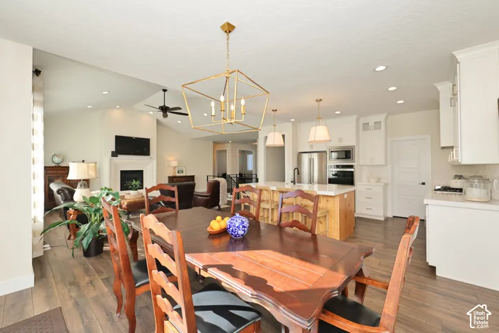 Open-concept kitchen featuring a center island with natural wood cabinetry and a stone countertop, complemented by white cabinetry, stainless steel appliances, geometric pendant lighting, and wood-finish flooring