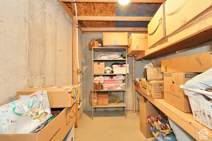 Storage room featuring unfinished concrete walls, exposed wood framing, and built-in wood shelving
