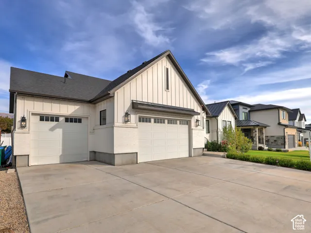 Board-and-batten exterior siding, concrete driveway, and attached three-car garage featuring panel-style doors with glass inserts and wall-mounted exterior lanterns