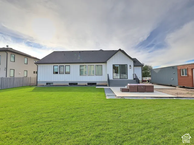 Exterior featuring white vertical siding, dark shingle roof, expansive manicured lawn, concrete patio, and stairs with metal railings