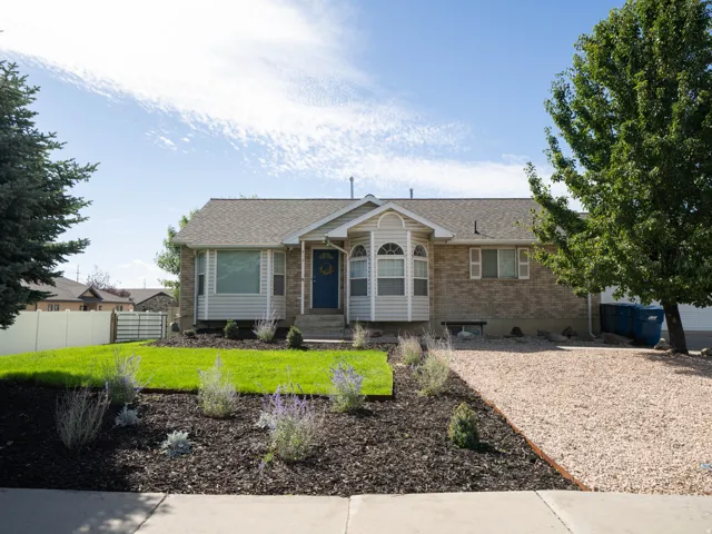 Brick and siding exterior with a bay window, gravel driveway, and landscaped front yard with mature trees
