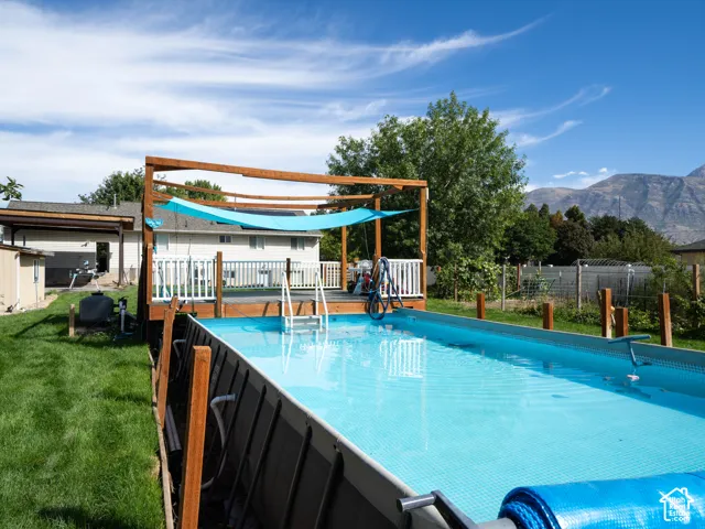 Expansive outdoor living area featuring an above-ground pool, a wooden deck with white railings, and a wooden pergola structure