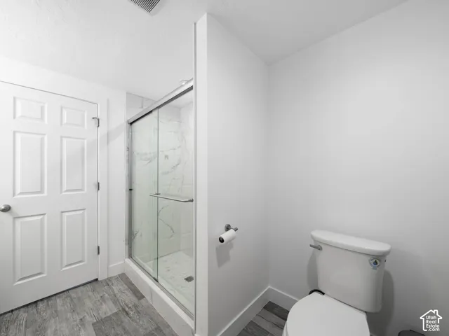 Glass-enclosed shower with white tiled surround, wood-finish flooring, and a white six-panel door
