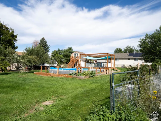 Expansive backyard featuring a large lawn, an above-ground swimming pool, a multi-level wooden deck with a shade canopy, and raised garden beds