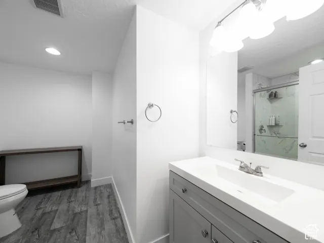 Bathroom featuring wood-finish flooring, a contemporary vanity with an integrated sink, a rectangular mirror, and an enclosed shower with tile surround
