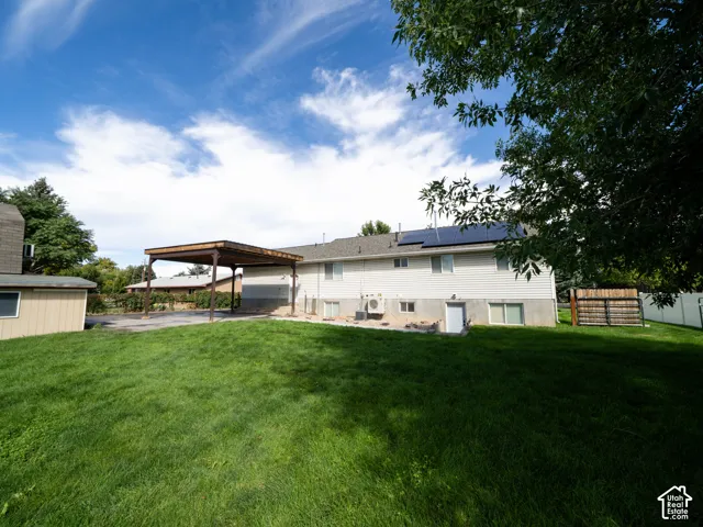 Expansive grass lawn with a covered carport structure, a storage shed, and solar panels installed on the roof